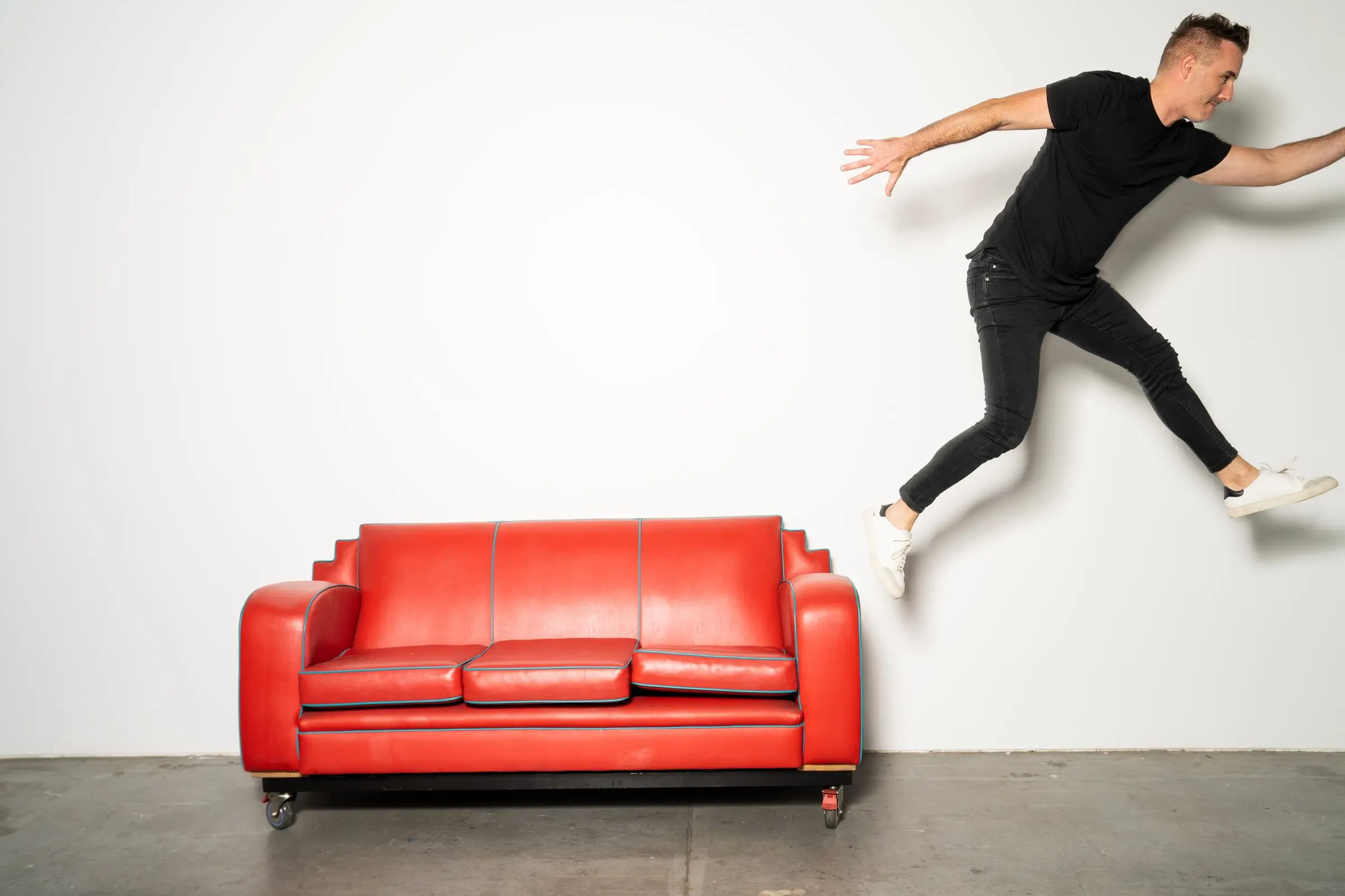 A tekFinder team member jumping over a red vintage sofa in a white studio